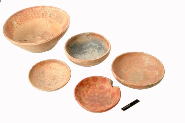 Four shallow bowls, a small dish, and an obsidian blade.