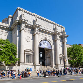 Central Park West Museum facade in the spring with a crowd of people lined up along the sidewalk.