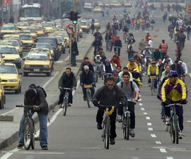 A large street, on the left side of a divider taken up with cars and trucks and on the right, full of people on bikes.