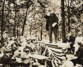 Theodore Roosevelt, standing on a platform, speaking to a crowd of people.