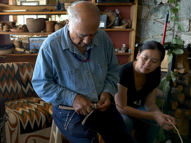 Suquamish Master Weaver Ed Carriere demonstrates splitting a cedar limb for conservator Amy Tjiong