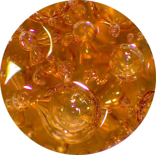 Brown silicate glass containing small to large spherical and elliptical gas bubbles.