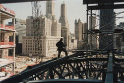 A man standing on the steel girder of a building high above a construction site with other New York City skyscrapers in the background.