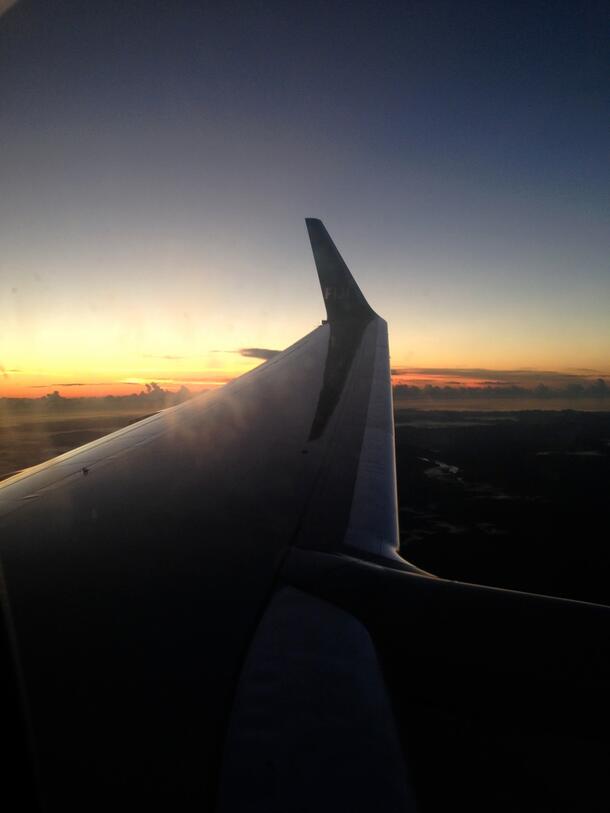 The wing of airborne plane at sunset as viewed by a passenger seated in the plane over the wing.