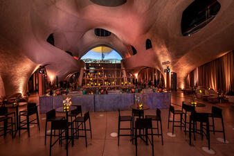 Small high tables and chairs and a large horse-shoe shaped bar inside the dramatically-lit atrium of the Richard Gilder Center.