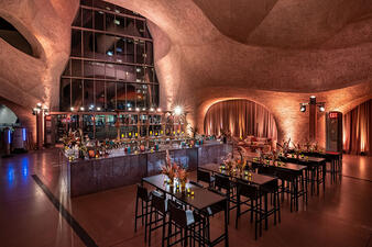 Small high tables and chairs and a large horse-shoe shaped bar inside the dramatically-lit atrium of the Richard Gilder Center.