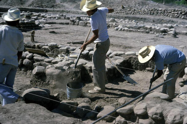 Three people with tools working in an arid dusty excavation site.