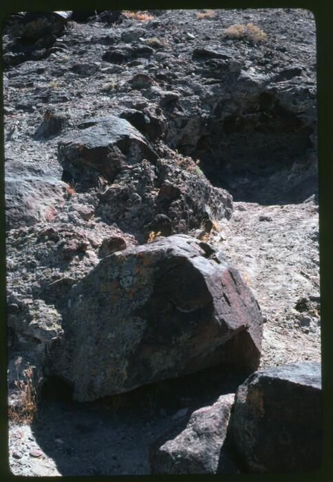 An outdoor photo of the entrance to an underground cave in Hidden Cave, Nevada. The ground surface is dry and rocky with large boulders and stones all around