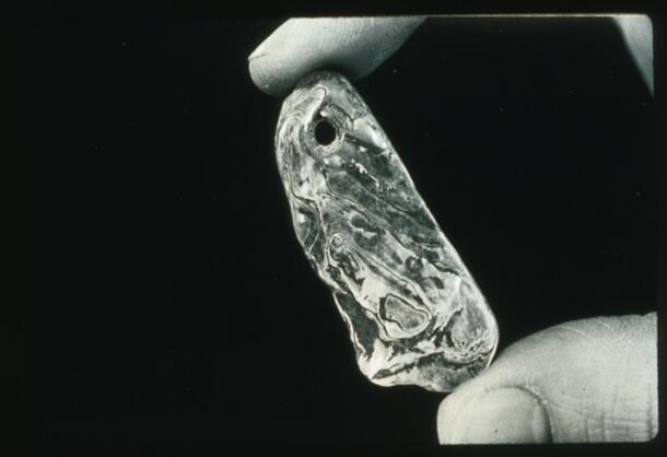 A hand holding a small flat artifact about 2 inches long with a small hole near the top.