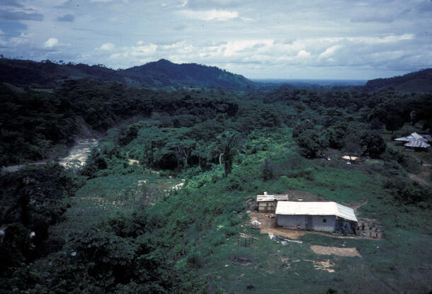 A small single-level house or research station on a flat green area with lush low green hills surrounding.