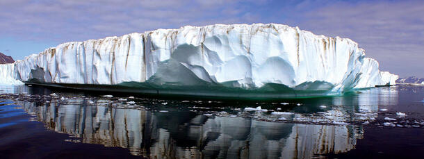 A tall, melting glacier reflected in the water.