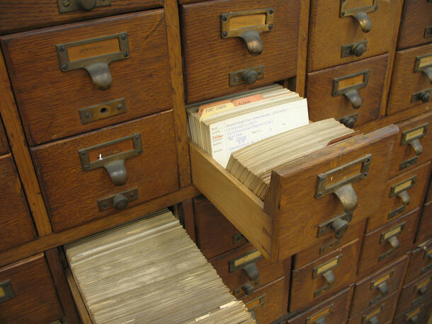Wooden drawers in a card catalog, two pulled out to reveal cards.