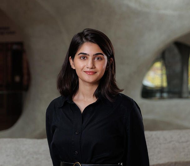 Samar Syeda stands for a smiling portrait with a view in the background of the curved walls of the Musuem's Gilder Center.