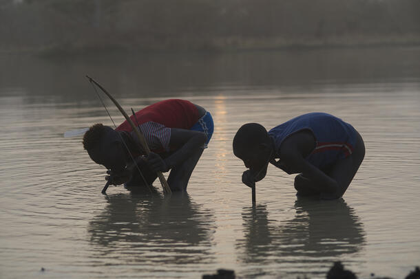 Two young African men standing in a lake and drinking lake water through large straws.