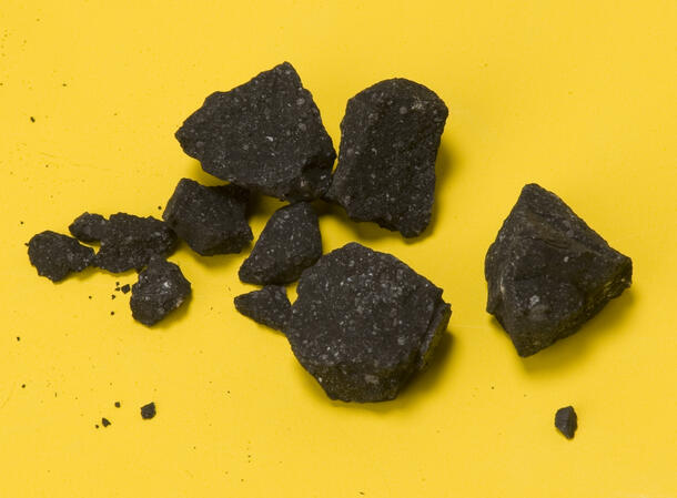 Meteor fragments, of irregular shape, dark with lighter specs. About a dozen are the size of small stones or pebbles. Ohers are very small, some like grains of sand.
