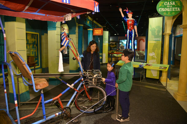 A reconstructed city boulevard emulating a street you might find in Cuba, with a family looking at a pedicab and a Carnival model in the background