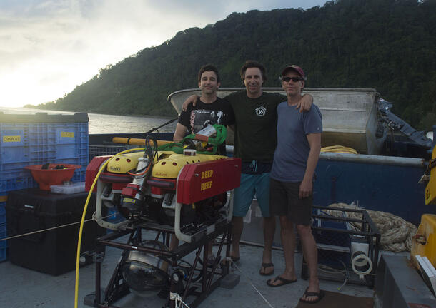 David Gruber, Brennan Phillips, and John Sparks stand on the deck of a boat surrounded by research equipment.