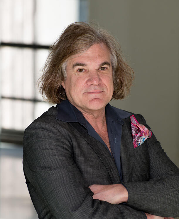Headshot of paleontologist Mark Norell with chin-length hair, wearing a suit and a colorful handkerchief in the front jacket pocket.