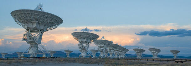 The many huge dishes of the Karl G. Jansky Very Large Array stand beneath a wide pastel sky.