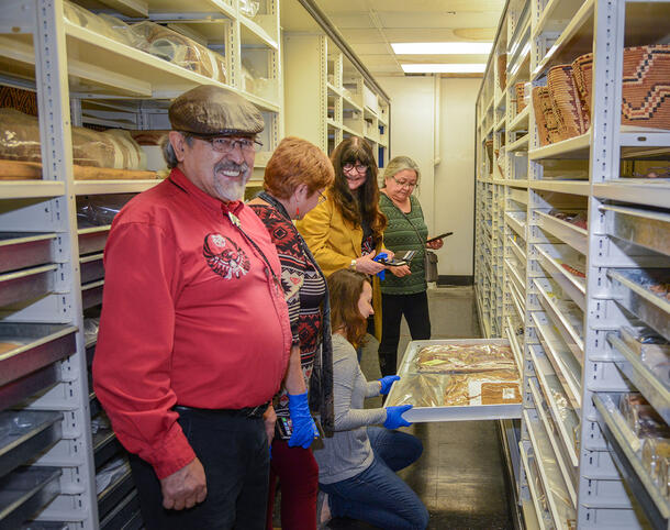 Ronald Ignace, Freda Jules, Marianne Ignace, and Jeanette Jules stand next to shelving in the Museum’s collection that contains ethnographic objects.