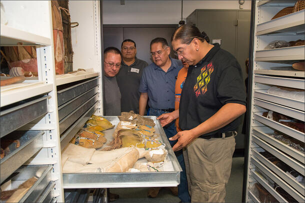 Five people stand over an open collections drawer holding pairs of moccasins. 