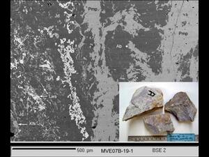 A field of gray color mottled with areas of darker gray and white, and a small superimposed photo of three gray rock specimens.