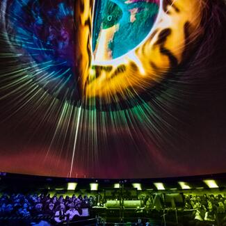 Audience sitting in planetarium theater looking up at the screen showing a planet.