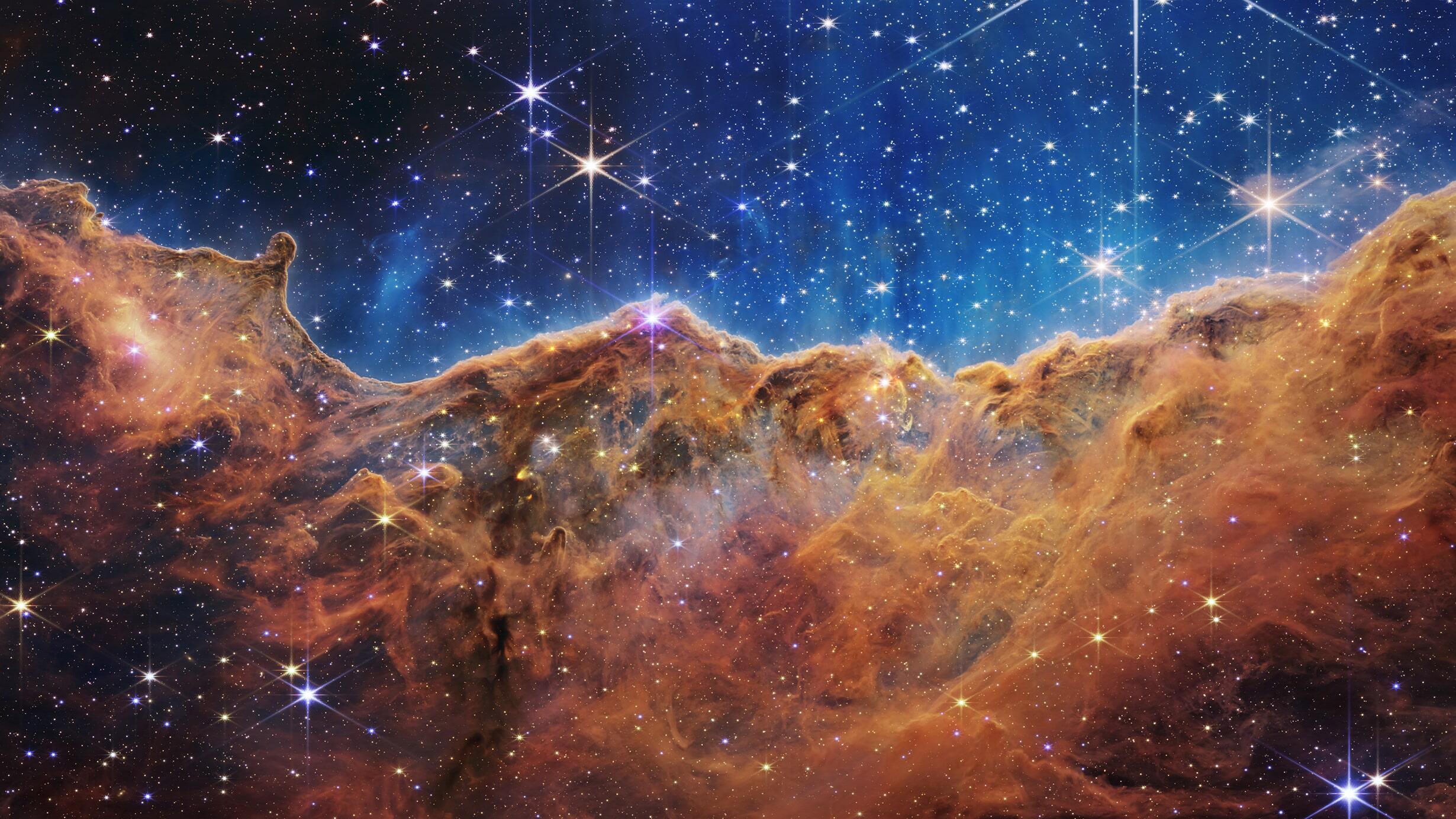The Carina Nebula - a milky sea of dark brown against a vivid blue expanse, stars shining through - photographed by the James Webb telescope in 2022.