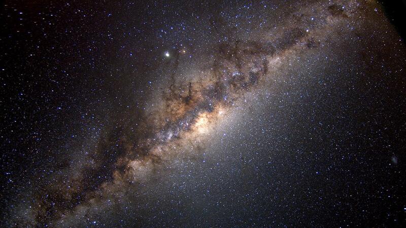 A depiction of the Milky Way galaxy, with billions of stars bright against a deep black sky, and a brilliant white cluster at its center.