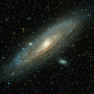 A photograph of the Andromeda Galaxy: brilliant colored stars against a sheer black foreground, with a thick, spiral disc at its center.