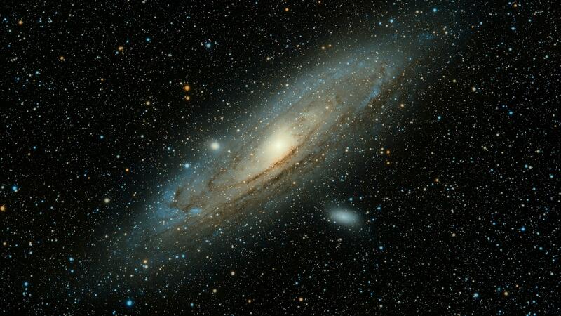 A photograph of the Andromeda Galaxy: brilliant colored stars against a sheer black foreground, with a thick, spiral disc at its center.