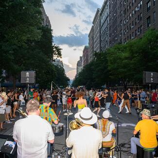 A salsa band performing in a street festival, with dancers enjoying a wide, blocked-off city avenue.