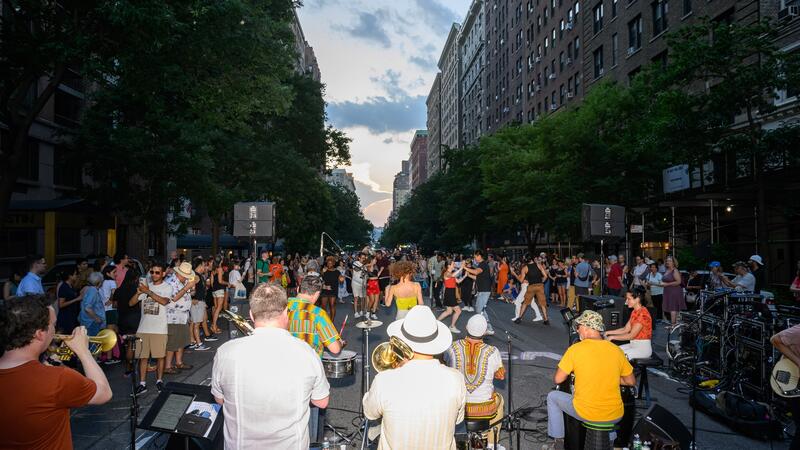 A salsa band performing in a street festival, with dancers enjoying a wide, blocked-off city avenue.
