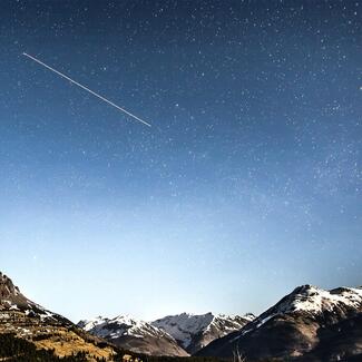 A meteorite over a mountain range at night, appearing as a bright streak of light against a rich background of stars. 