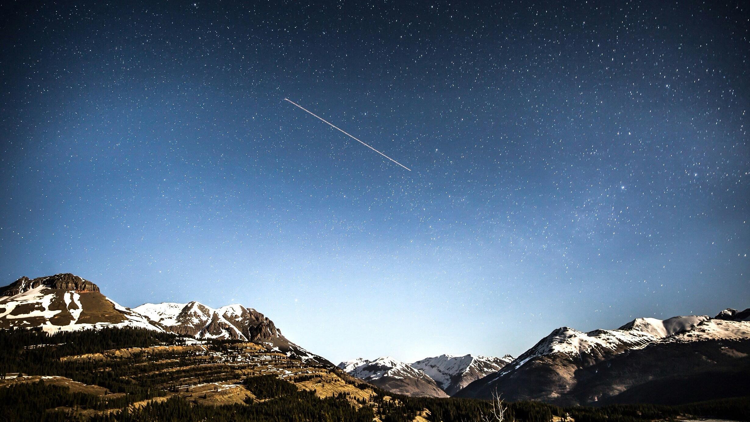 A meteorite over a mountain range at night, appearing as a bright streak of light against a rich background of stars. 