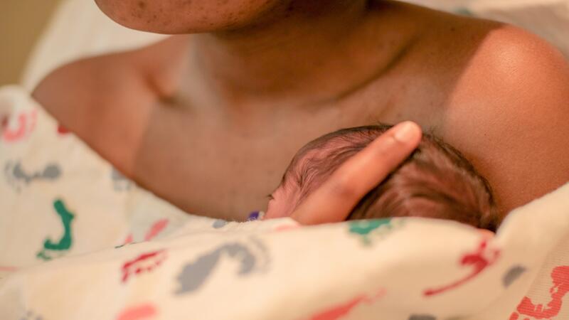 A newborn infant, covered in a blanket and resting on their mother's chest.