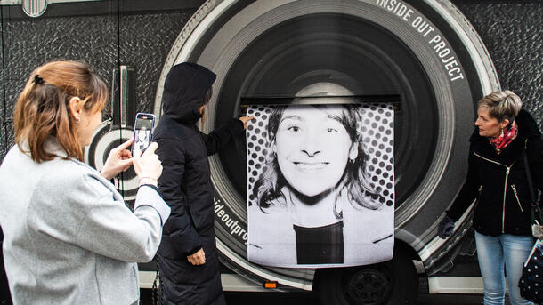 Person takes a photo with their cellphone of a person holding a large photo print as it is being expelled through a printer on the side of a photo truck.