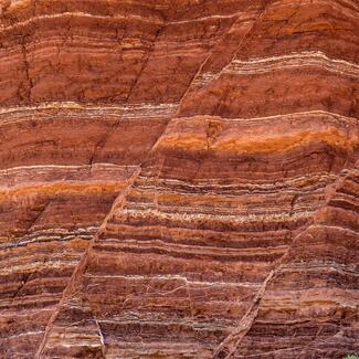 A sheer wall of reddish rock in the desert. Clearly delineated, horizontal layers with distinct coloration correlate with different geological eras.