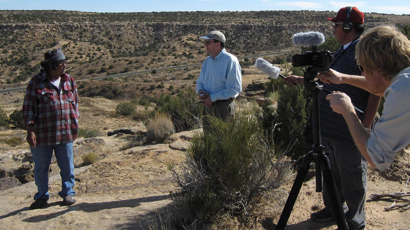 Harold Polingyumptewa and Peter Whiteley stand facing one another on top of rocky ridge, filmed by two camera men.