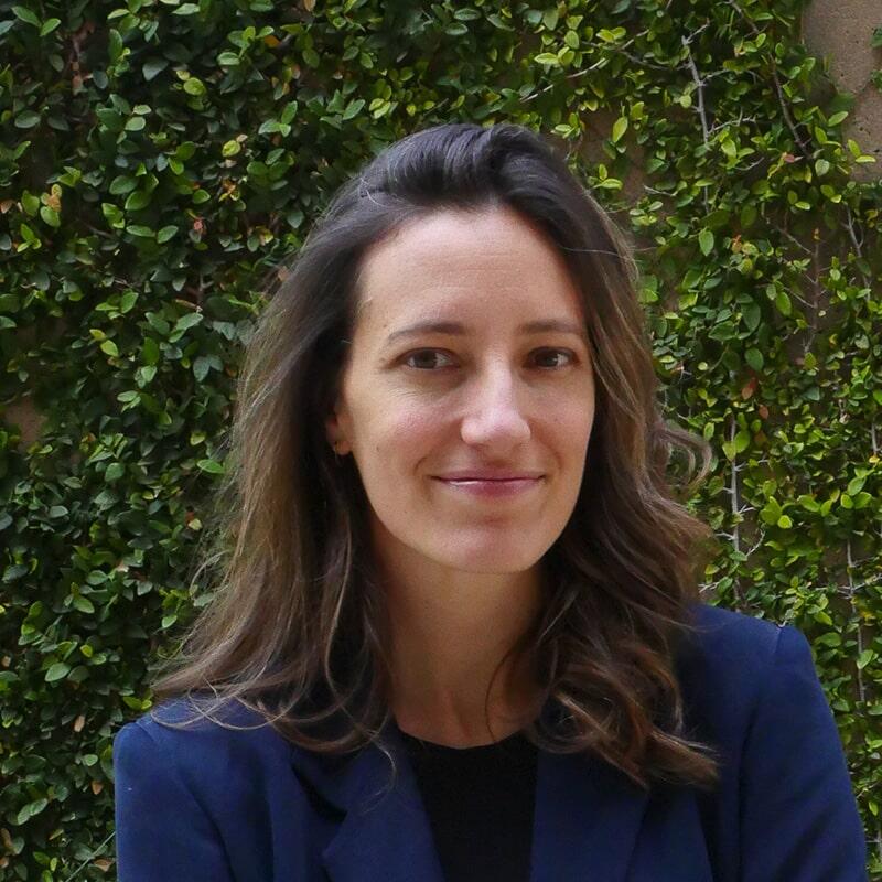 A portrait photograph of Holly Buck, arms folded with a wall of creeping vines in the background