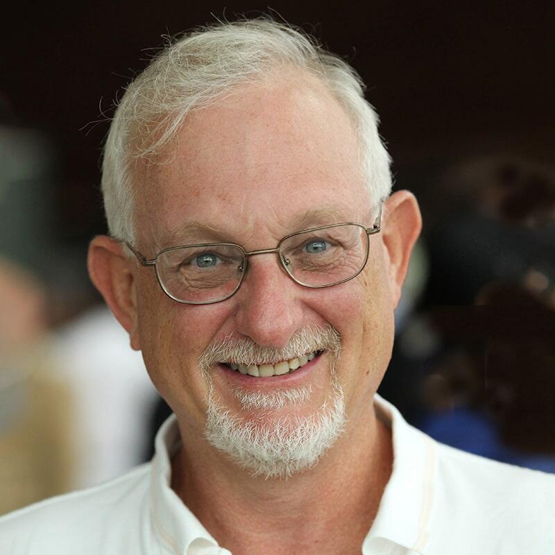 A close-up photograph of Howard Herzog, smiling in a white collared shirt.