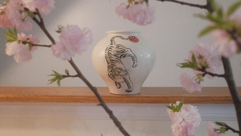 An example of Korean porcelain. A white glazed vase with an illustration of a tiger.  Branches with cherry blossoms appear in the foreground.