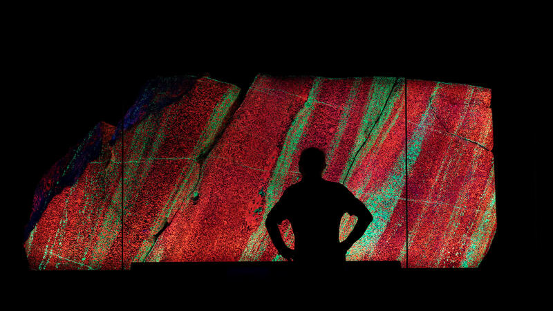 Dark silhouette of a Museum visitor against the backdrop of a large glowing slab of fluorescent granite.