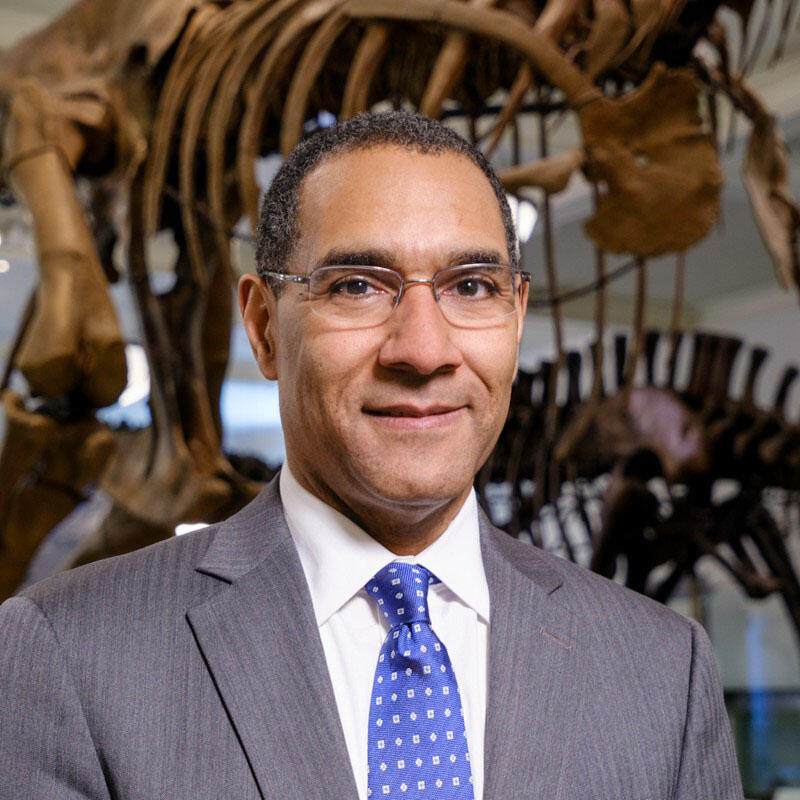 Smiling headshot of Sean M. Decatur, posed in front of a dinosaur fossil mount.