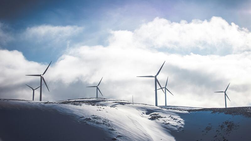 Large wind turbines, seen in the distance against a bright white snow-covered landscape.