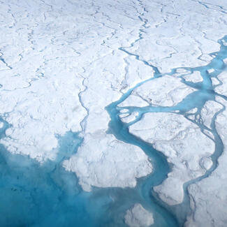 Aerial view of Greenland ice sheet shows rivers and ponds forming on the surface of the ice.