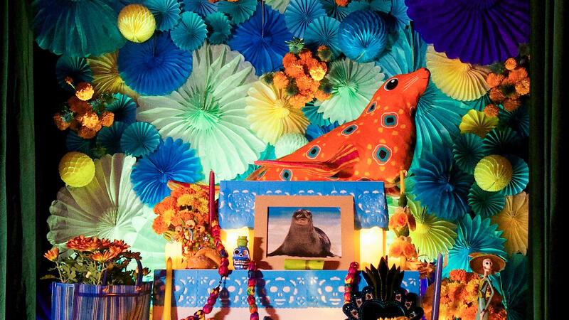 Sculpture and photo of a Caribbean monk seal surrounded by paper flowers, candles, beads and other offerings.