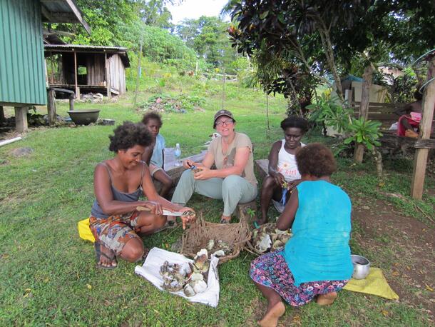 Dr. Georgina Cullman sits on the ground with four local people in the Solomon Islands, all shucking giant clams around two large woven baskets.