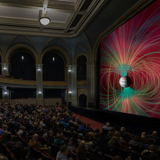 Seated Museum visitors inside the Lefrak Theater view a giant screen film adaptation of Worlds Beyond Earth.
