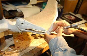 Two hands holding a tool and working on a small pterosaur model.
